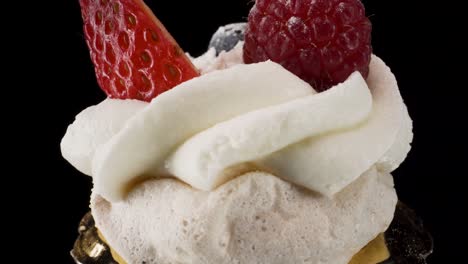 closeup-macro-view-turning-mini-pavlova-on-black-reflective-glass-background,-mini-luxury-patisserie,-sweet-dessert