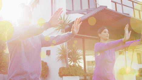 animation of spots of light over biracial couple practicing yoga by house