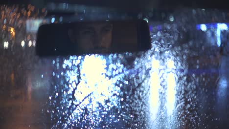 el joven se sienta en el coche en la noche lluviosa