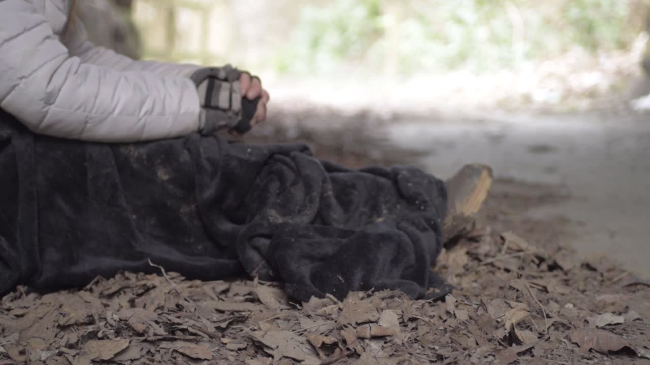 Homeless person wrapped up in dirty blanket rubbing hands to keep warm