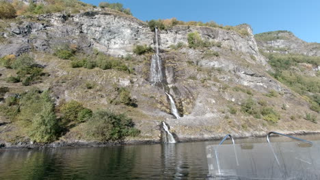 view of a tall waterfall flowing off of a mountain and into a fjord from a boat