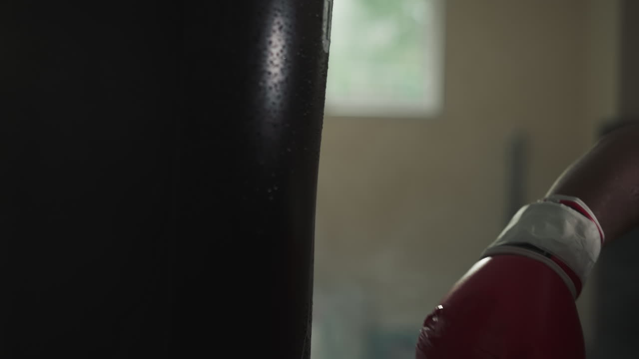 Boxing coach in gloves delivers powerful strike to punching bag in gym with equipment. Man specialist actively participates in sports and builds muscle mass