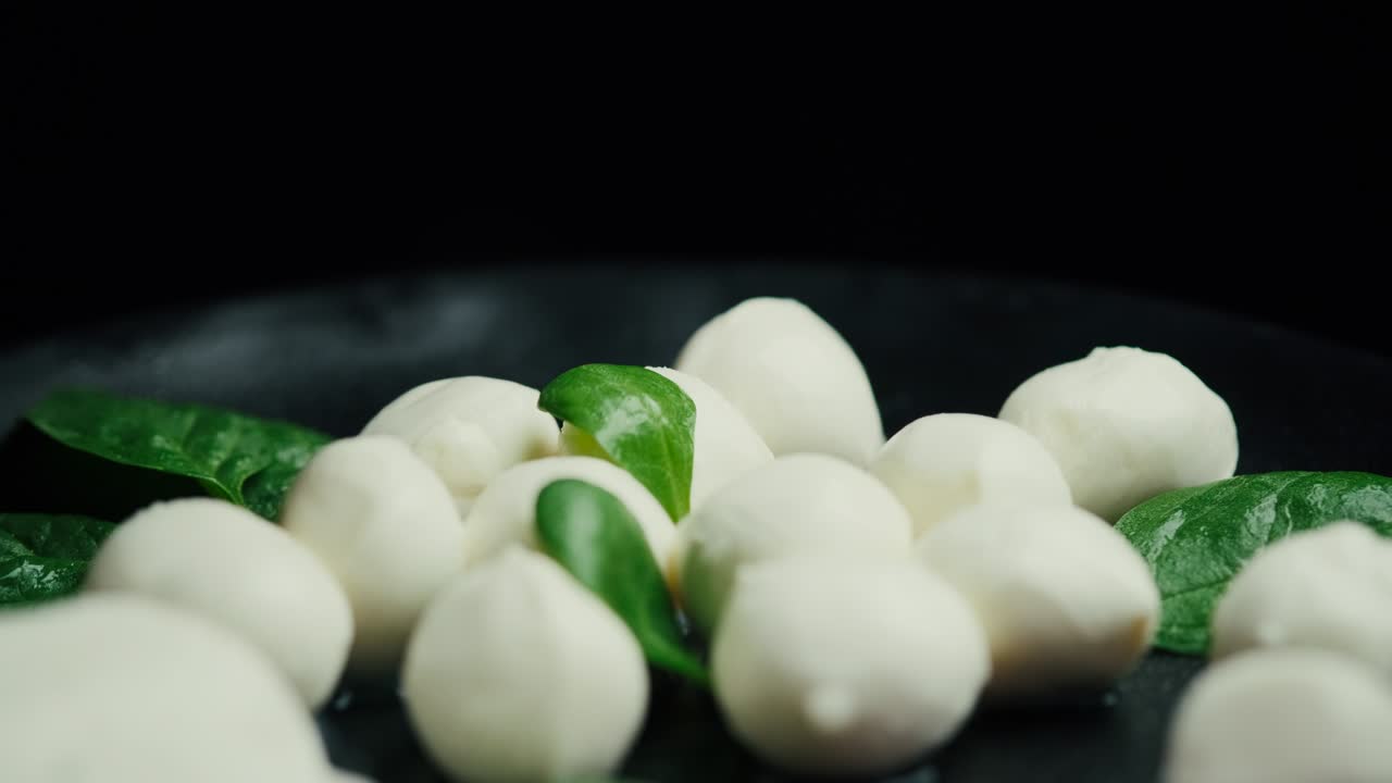 pequeñas bolas de queso mozzarella blanco, hojas de espinaca y tomates en un plato negro.