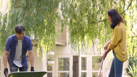 Mature-Asian-couple-working-in-garden-at-home-raking-leaves-into-barrow--shot-in-slow-motion