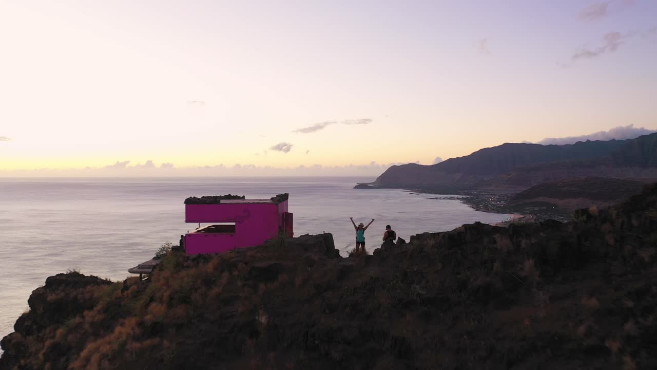 Aerial shot flying over Puu O Hulu mountain in Hawaii and two hikers waving at camera from the top. Dolly in