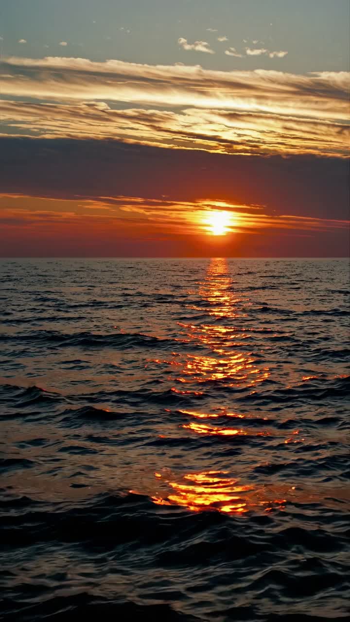 A serene sunset over the ocean, captured from a low angle. The video style emphasizes the warm hues