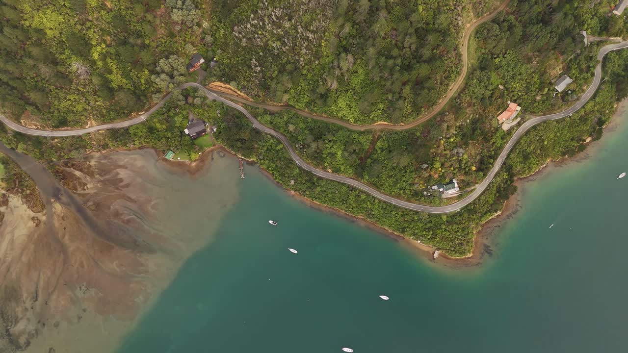 Coastal road with clear lake water and beach in picton area, New Zealand. Aerial top down shot. Boats cruising on water