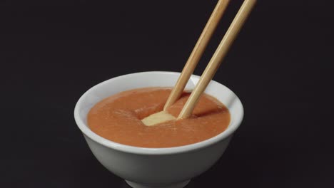 close up of tofu dipping to shabu shabu dip sauce by chopsticks on the black background