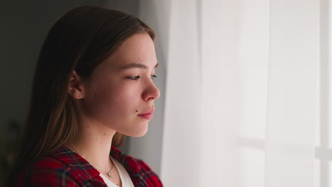 Depressed-woman-stands-looking-out-of-window-in-apartment