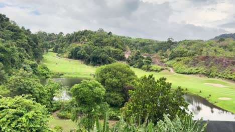 a serene view of a tropical golf course in phuket, thailand, showcasing vibrant greenery and rolling hills under a cloudy sky