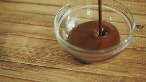 Hot-chocolate-pouring-into-glass-bowl-standing-on-wooden-table.