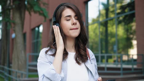 caucasian student woman wearing headphones and listening to the music on smartphone while walking down the street