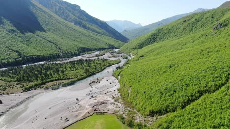 drone view in albania in the alps flying over a crystal river with rocky ground with green forest on the sides in theth