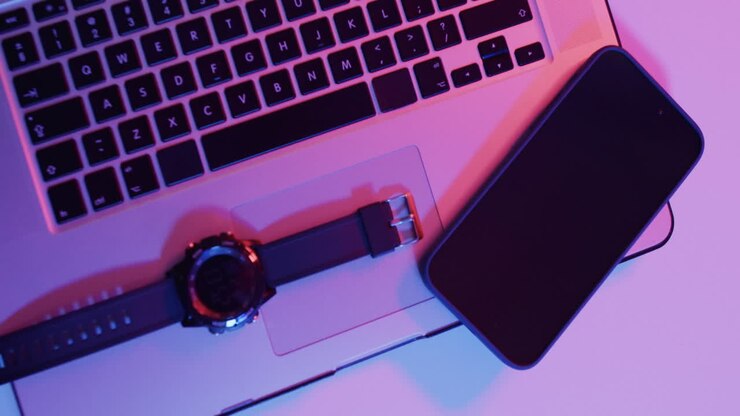 Video of laptop, smartphone and smartwatch on desk with copy space on neon background