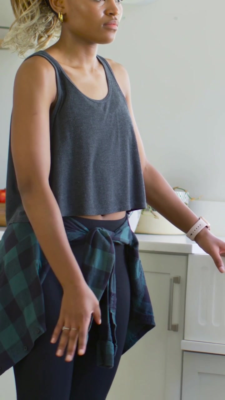 Vertical video: Reaching woman moving arms toward offframe in kitchen, flannel tied, smartwatch