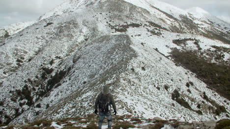 Rear-view-of-mountain-climber-on-top-of-snowy-white-Monte-Linas-peak-in-Sardinia-followed-by-german-Sheperd-dog,-Italy,-wide-shot,-zoom-in