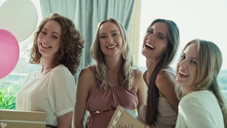 grupo de mujeres caucásicas con regalos en la fiesta del bebé mirando al lado de la cámara.