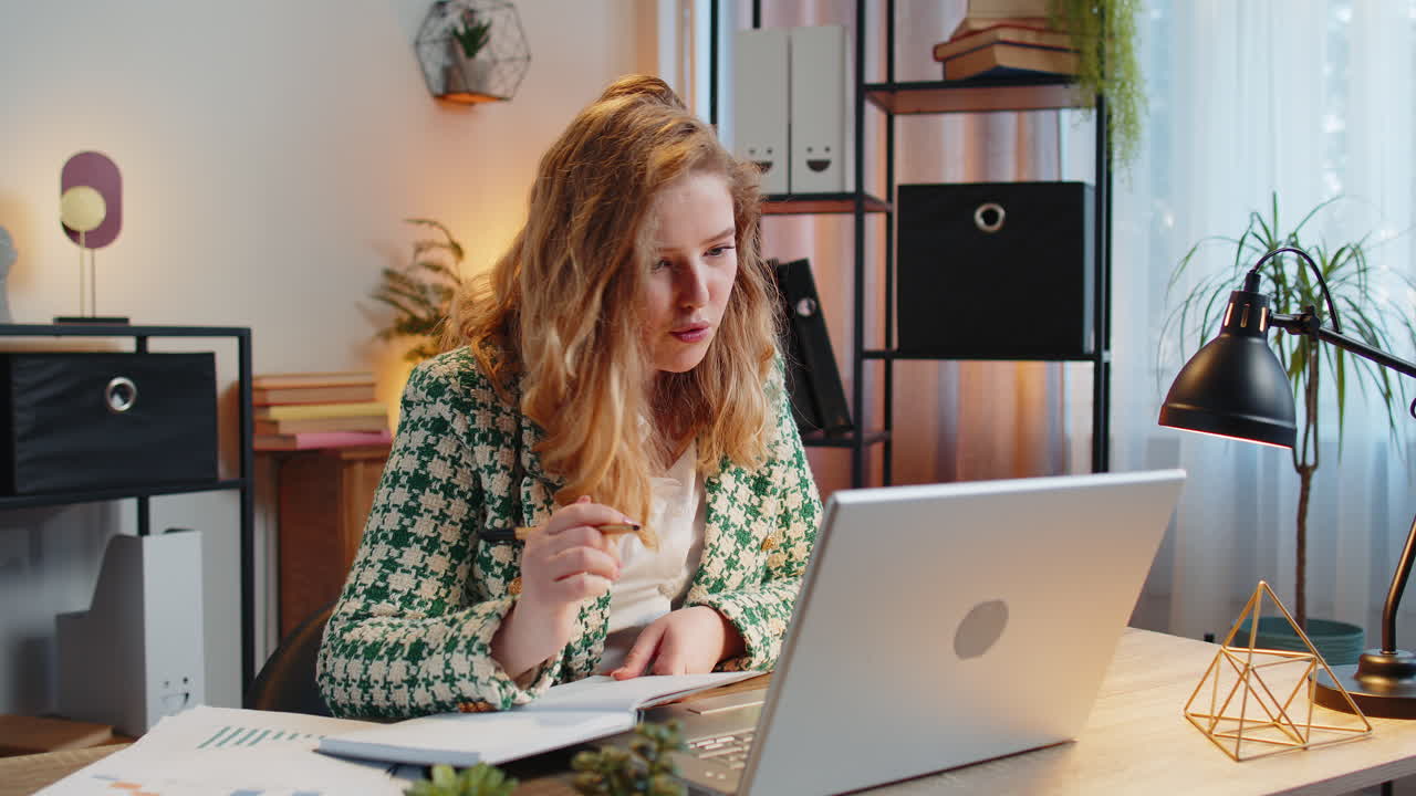Business woman writing down taking down notes while attending online video class meeting on laptop