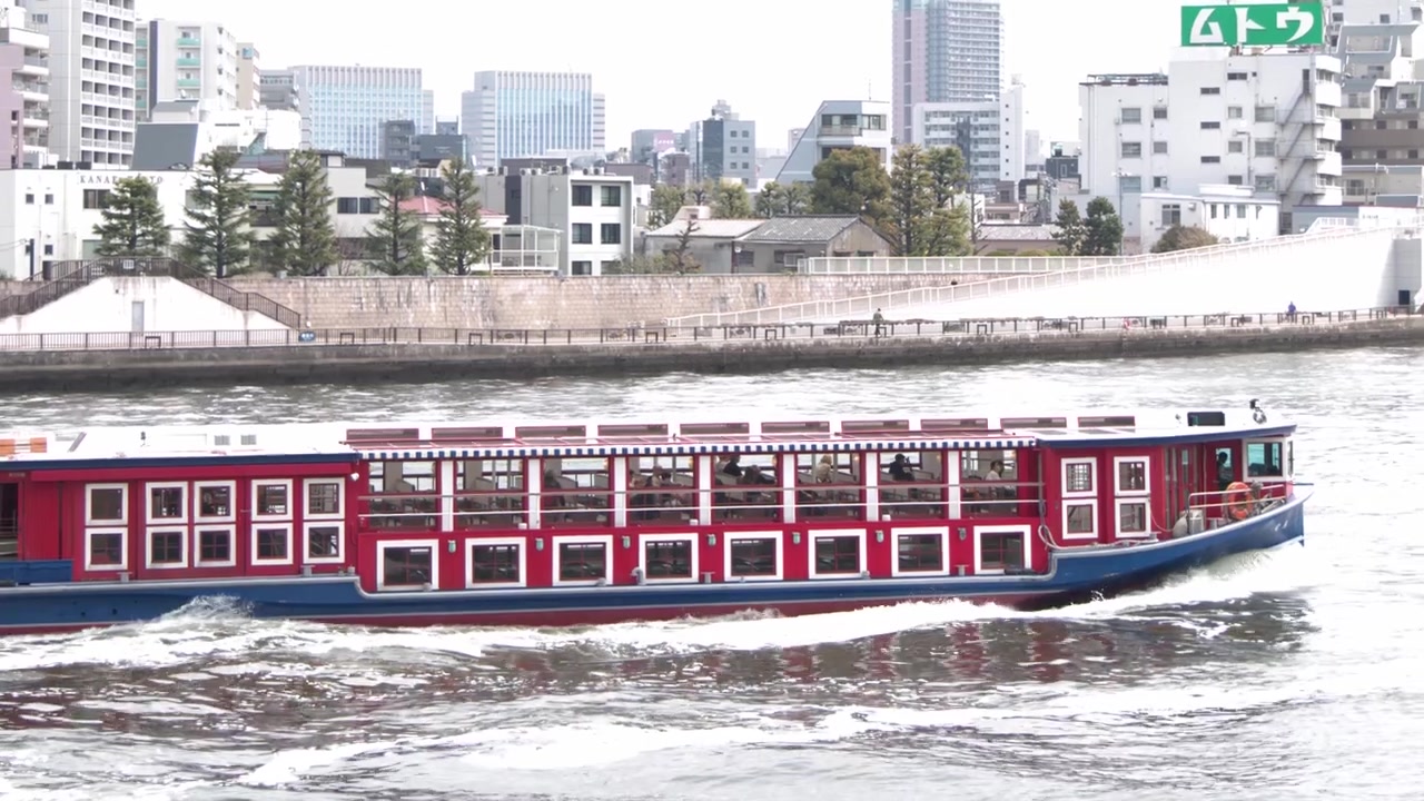 Un taxi acqueo rosso naviga lungo il fiume Sumida con l'architettura della città di Tokyo sullo sfondo.