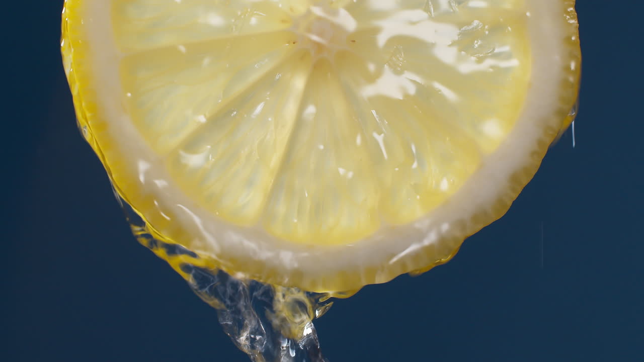 파란색 검정색 배경에 있는 레몬 슬라이스에서 흐르는 물의 슬로우 모션 매크로 샷
