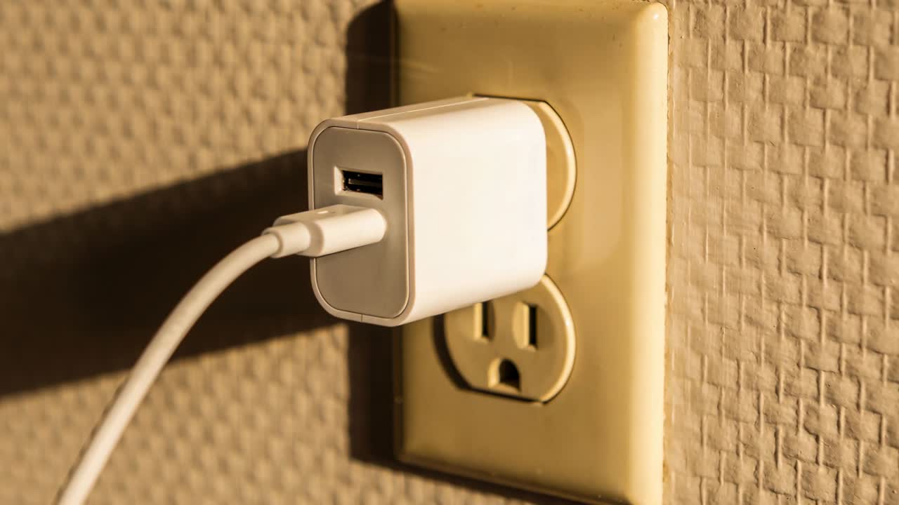Casting warm left light, white USB adapter staying plugged into beige outlet, cable casting shadow