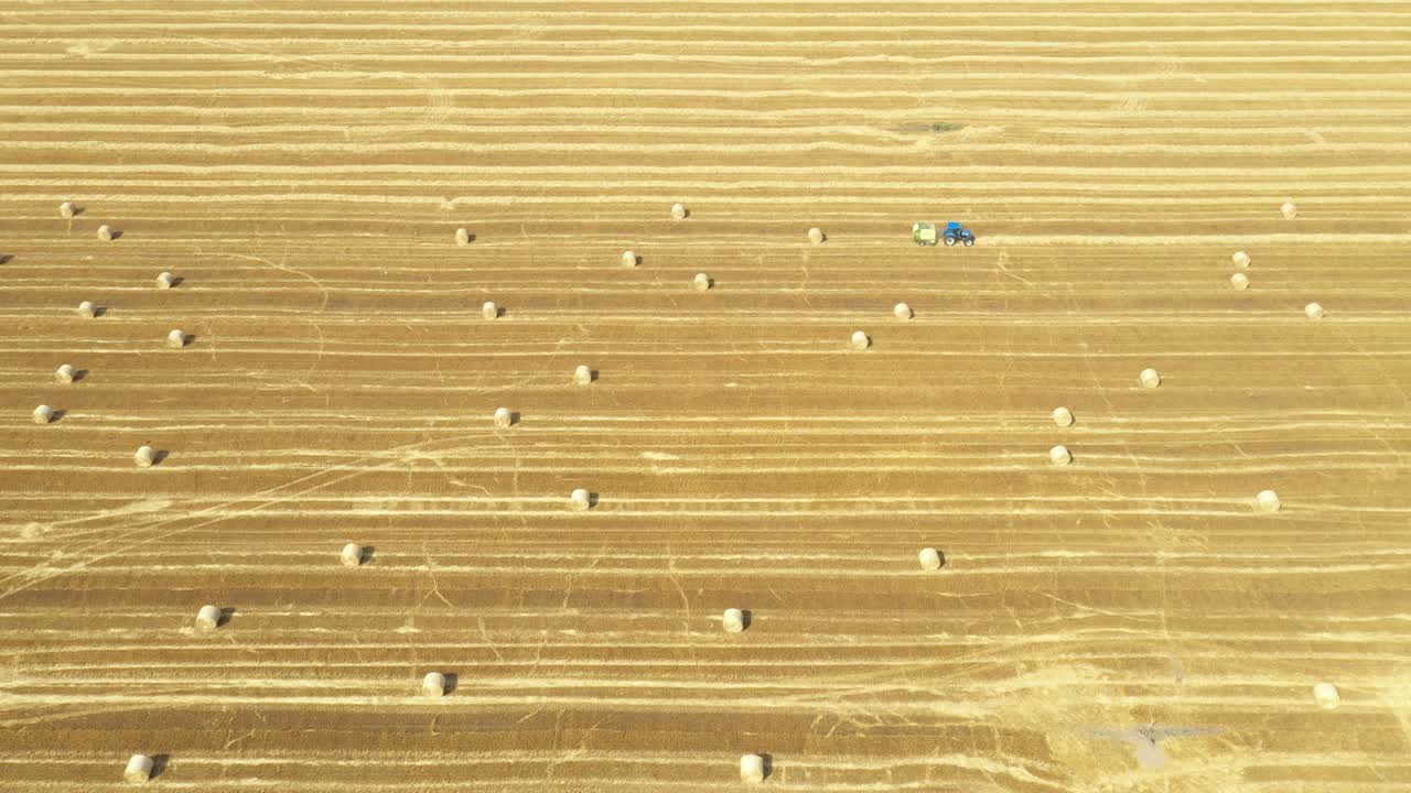 Aerial view of tractor tow trailed bale machine to collect straw from harvested field