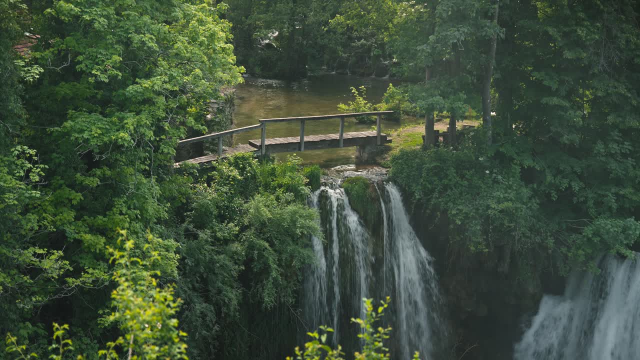 Bellissima doppia cascata con una passerella di legno e una vegetazione lussureggiante a Rastoke, Croazia