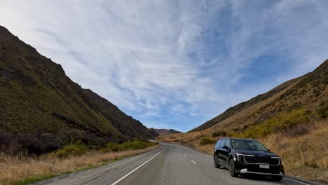 a serene drive through mountainous terrain in new zealand, showcasing autumn colors under a partly cloudy sky