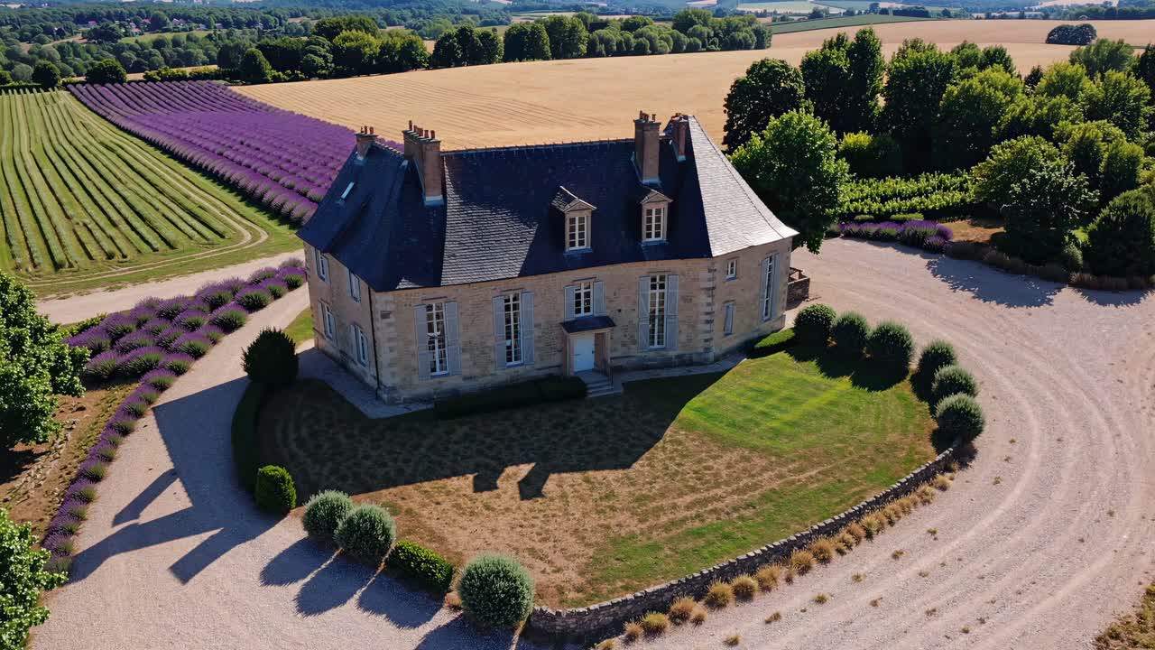 Aerial view of a beautiful French manor house surrounded by blooming lavender fields, golden wheat fields, and lush greenery, creating a picturesque rural landscape in the French countryside