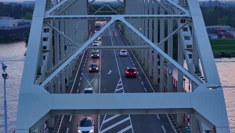 as sun is setting a busy queue of traffic crosses over a large steel bridge