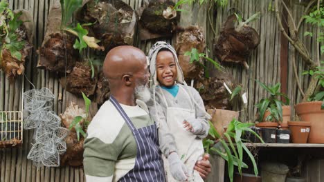 Portrait-of-happy-senior-african-american-man-with-his-grandson-embracing-and-smiling-in-garden