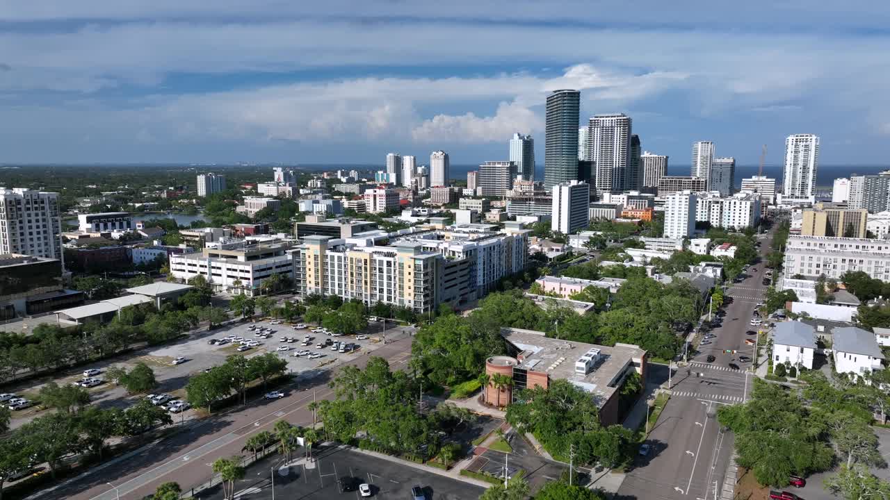 Aerial shot of parking area with cars and skyline of St. Petersburg, Florida. Downtown of city with straight streets and modern buildings. Gulf of Mexico or American in distance. Descend wide shot.