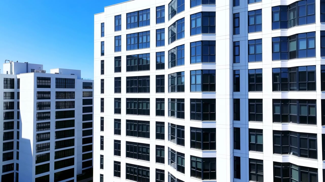 Alti edifici per uffici contemporanei con facciate bianche e in vetro si ergono in piena luce diurna, mostrando riflessi nitidi, linee pulite e un forte skyline urbano.