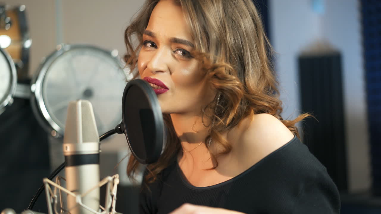 Young female singer recording album in the professional studio. Woman singing a song in music recording studio.