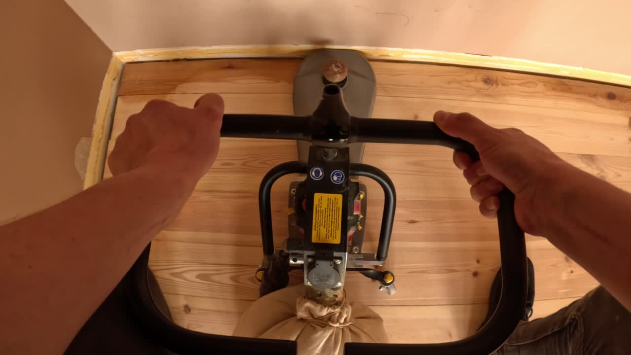 POV of a contractor guiding a floor sander across wooden planks, moving forward to smooth the surface during a detailed renovation pass