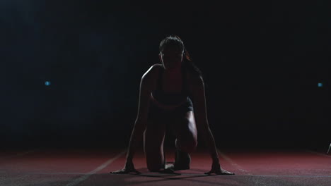 Young-woman-athlete-in-black-shorts-and-a-t-shirt-is-preparing-to-start-in-the-race-for-100-meters-on-the-treadmill-near-the-start-line