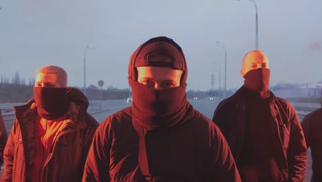 group of young men in balaclavas with red burning signal flare on the road