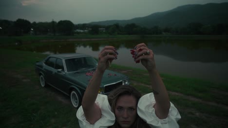 woman by a vintage car near a lake at dusk