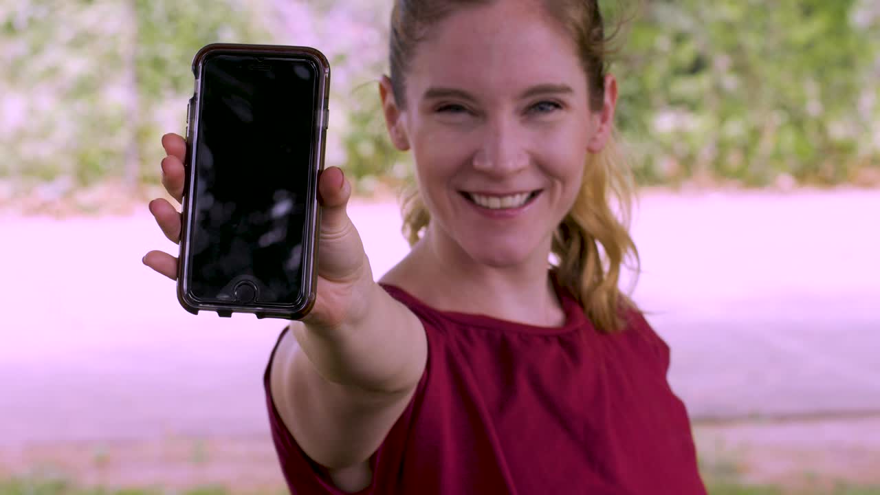 mujer feliz sonriente mostrando la pantalla de su teléfono móvil y apuntando a ella