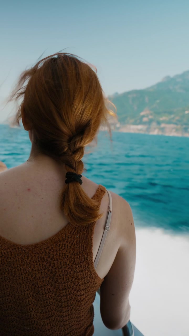 Woman with a braided ponytail facing the coastline from a speedboat