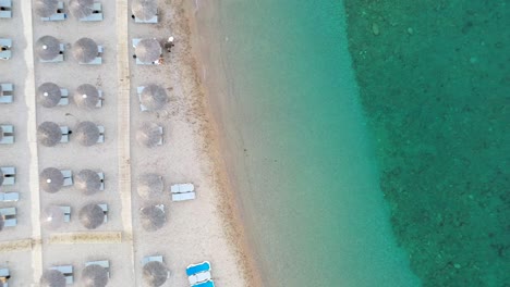 Aerial-view-of-sea-waves,-umbrellas-on-the-sandy-beach-at-sunrise