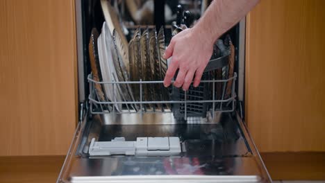 man hand loading dishes into dishwasher and closing it