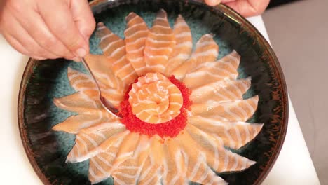 food plating - chef with teaspoon putting red caviars around the sashimi salmon rose on a round plate