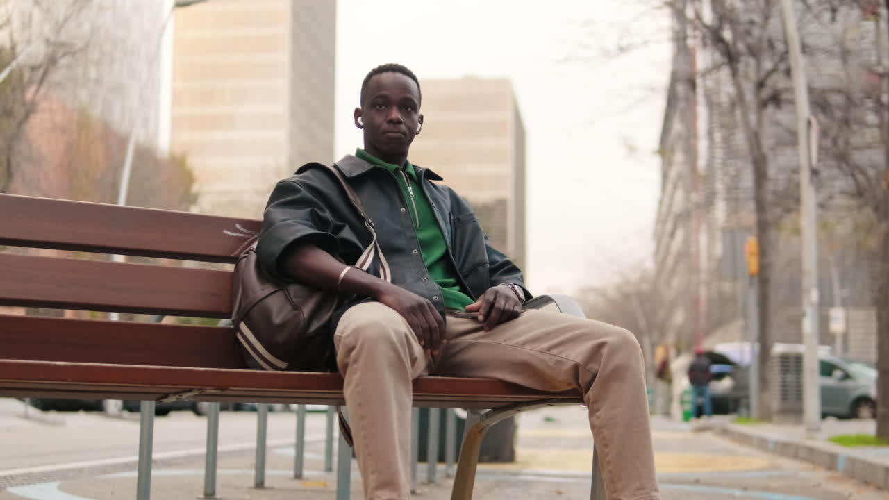 Jeune homme noir assis sur un banc de parc en ville.