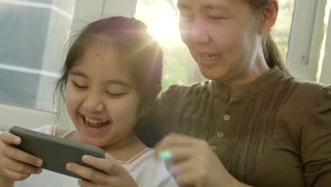 4k asian girl playing games on smart phone with her mother, happy time together