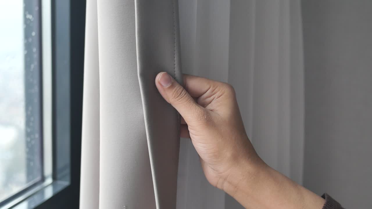 Person richtet einen Vorhang am Fenster zurecht