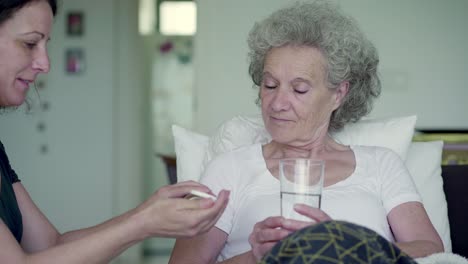 Lächelnde-Reife-Frau,-Die-Der-Kranken-Mutter-Ein-Glas-Wasser-Und-Pillen-Gibt.