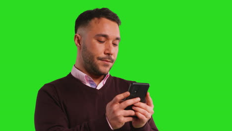 fotografía de estudio de cerca de un hombre de negocios que usa un teléfono móvil para enviar mensajes o navegar en línea de pie contra una pantalla verde