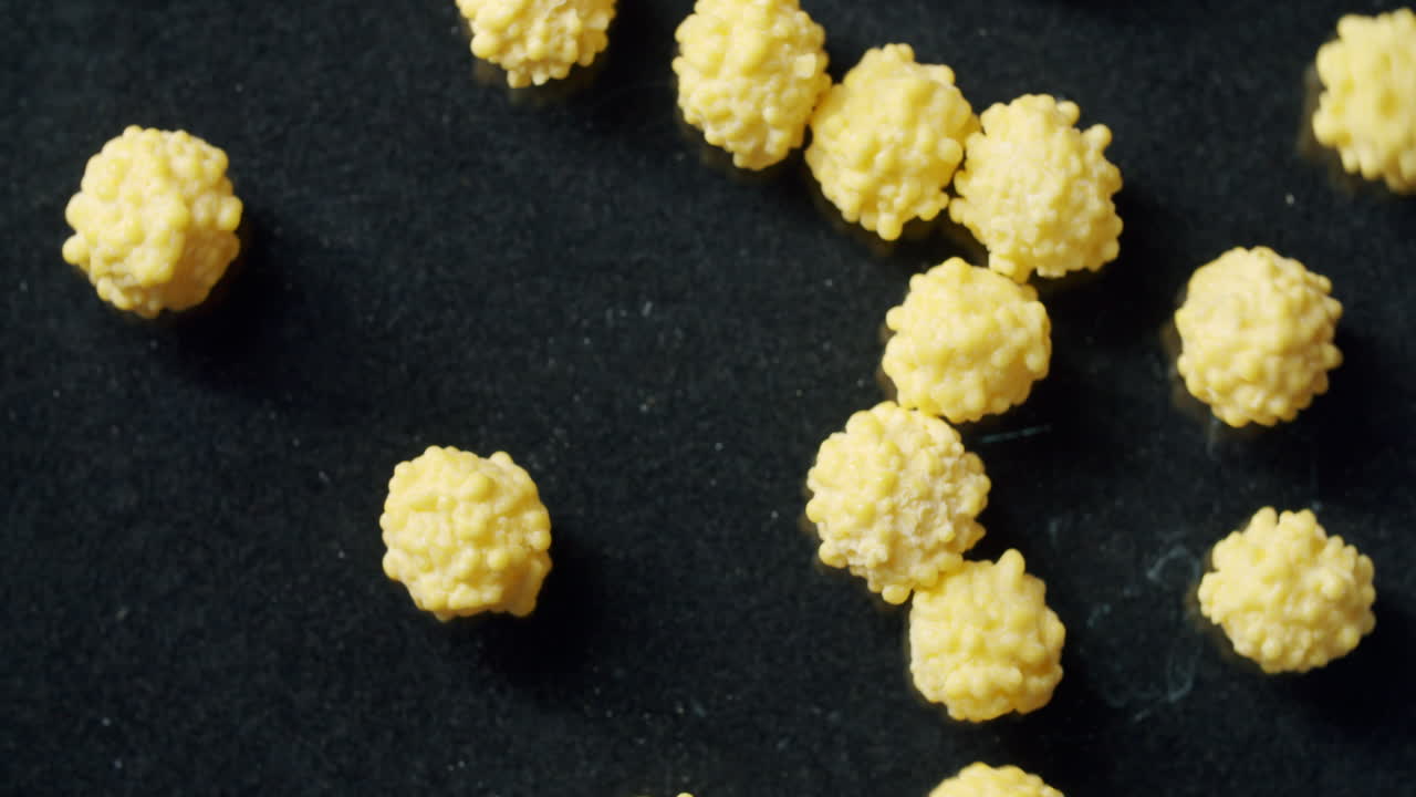 Looking through a microscope at yellow virus cells on a black surface. Black surface spinning clockwise. Light from the left side