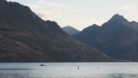 Una-Lancha-Parece-Pequeña-Contra-El-Majestuoso-Telón-De-Fondo-De-Las-Montañas-En-Queenstown,-Nueva-Zelanda